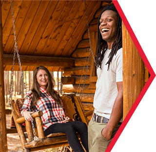 A couple standing outside a camping cabin laughing.