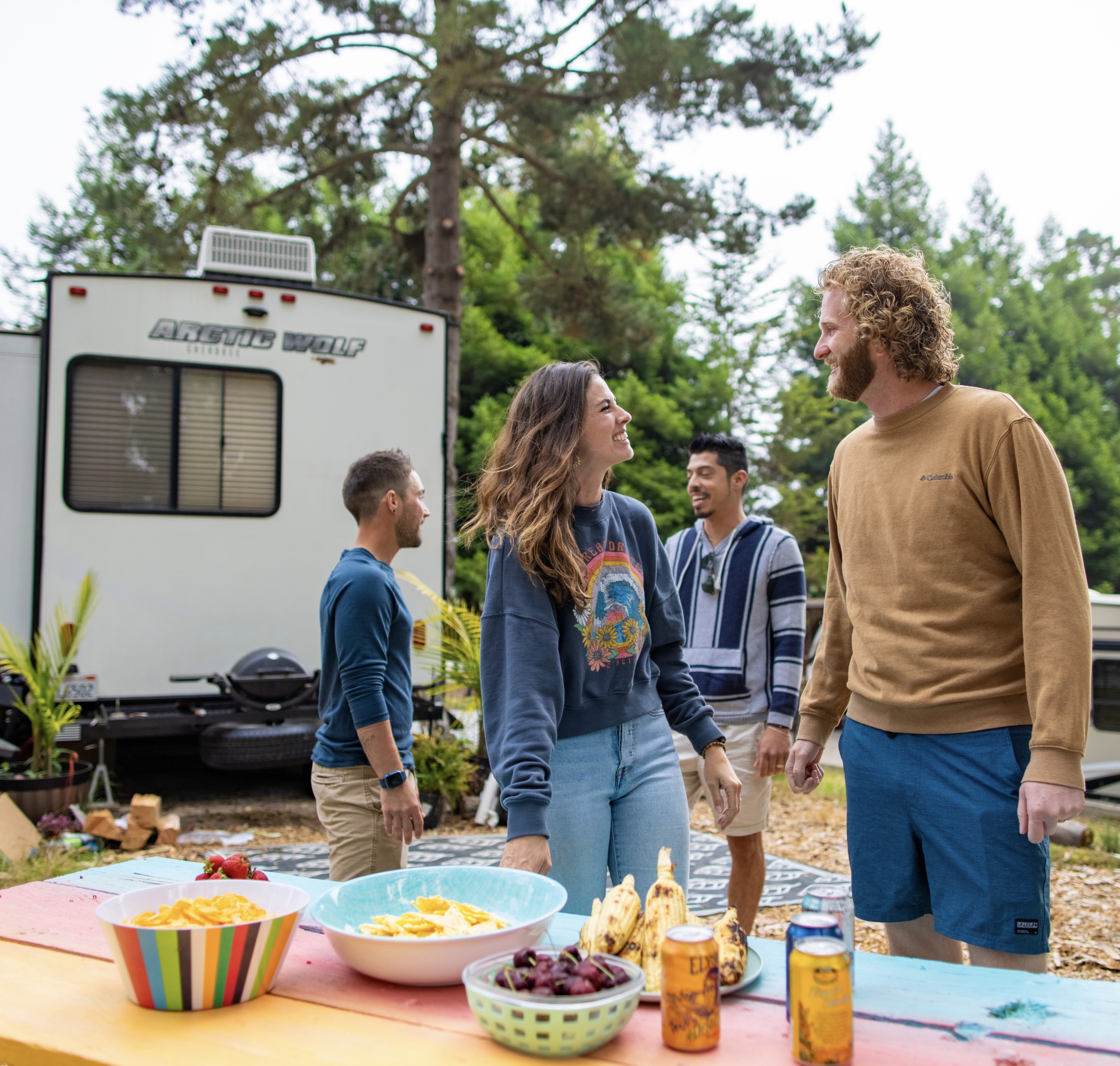 Four friends at a KOA campsite eating snacks with an RV in the background.