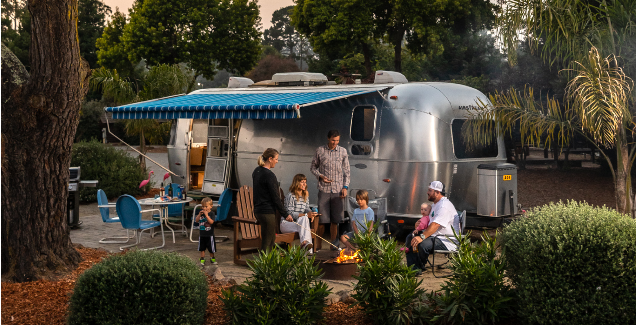 Friends sitting around a campfire outside their Airstream at a KOA campground.