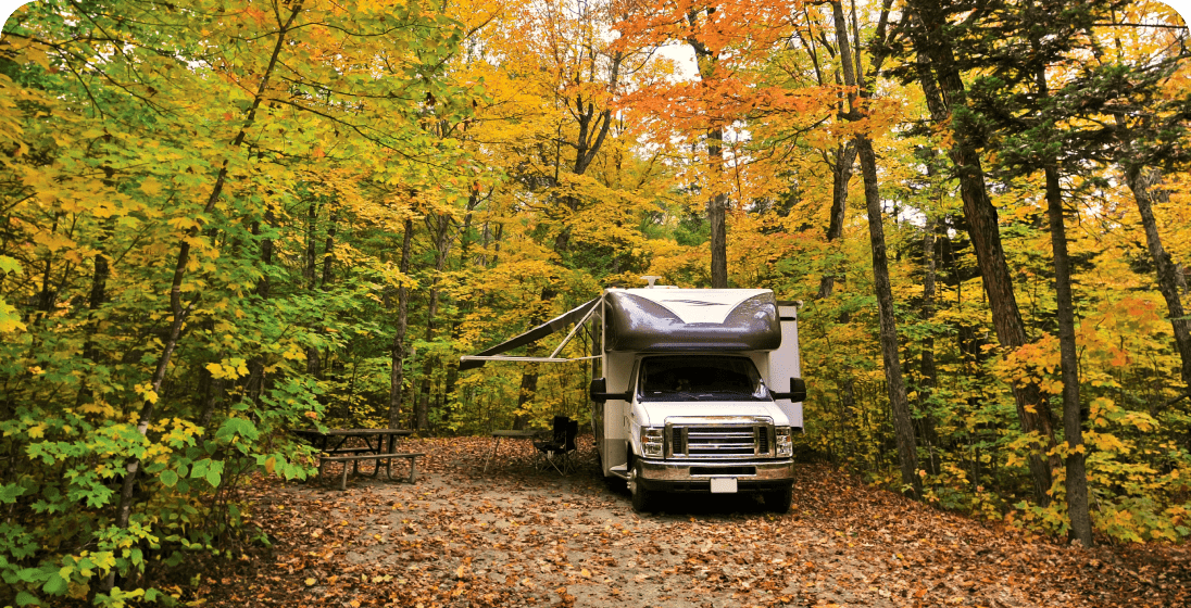 An RV setup in the woods with fall foliage.