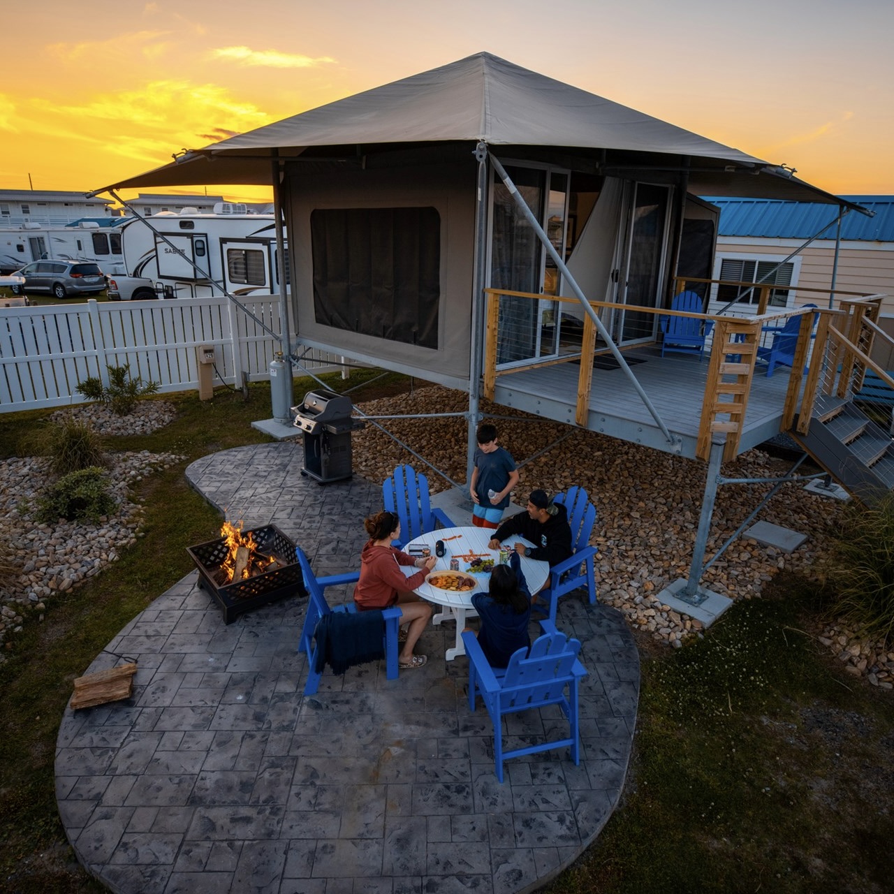 A group of people sitting outside of an eco-glamping tent at sunset.