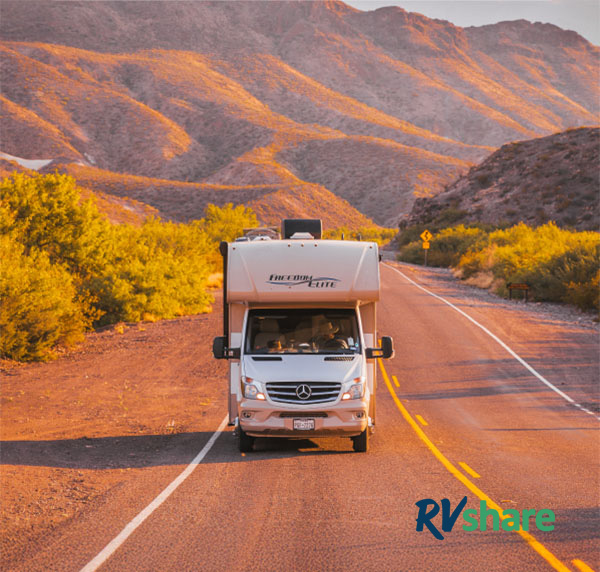 An RV driving down a road with mountains in the background during the daytime.